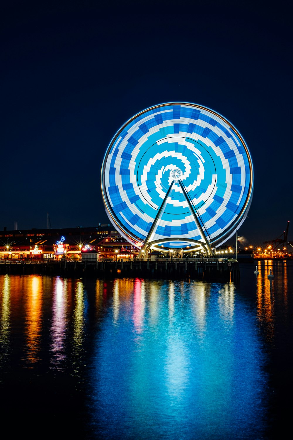 Ruota panoramica con luce LED blu che si riflette sullo specchio d'acqua durante la notte