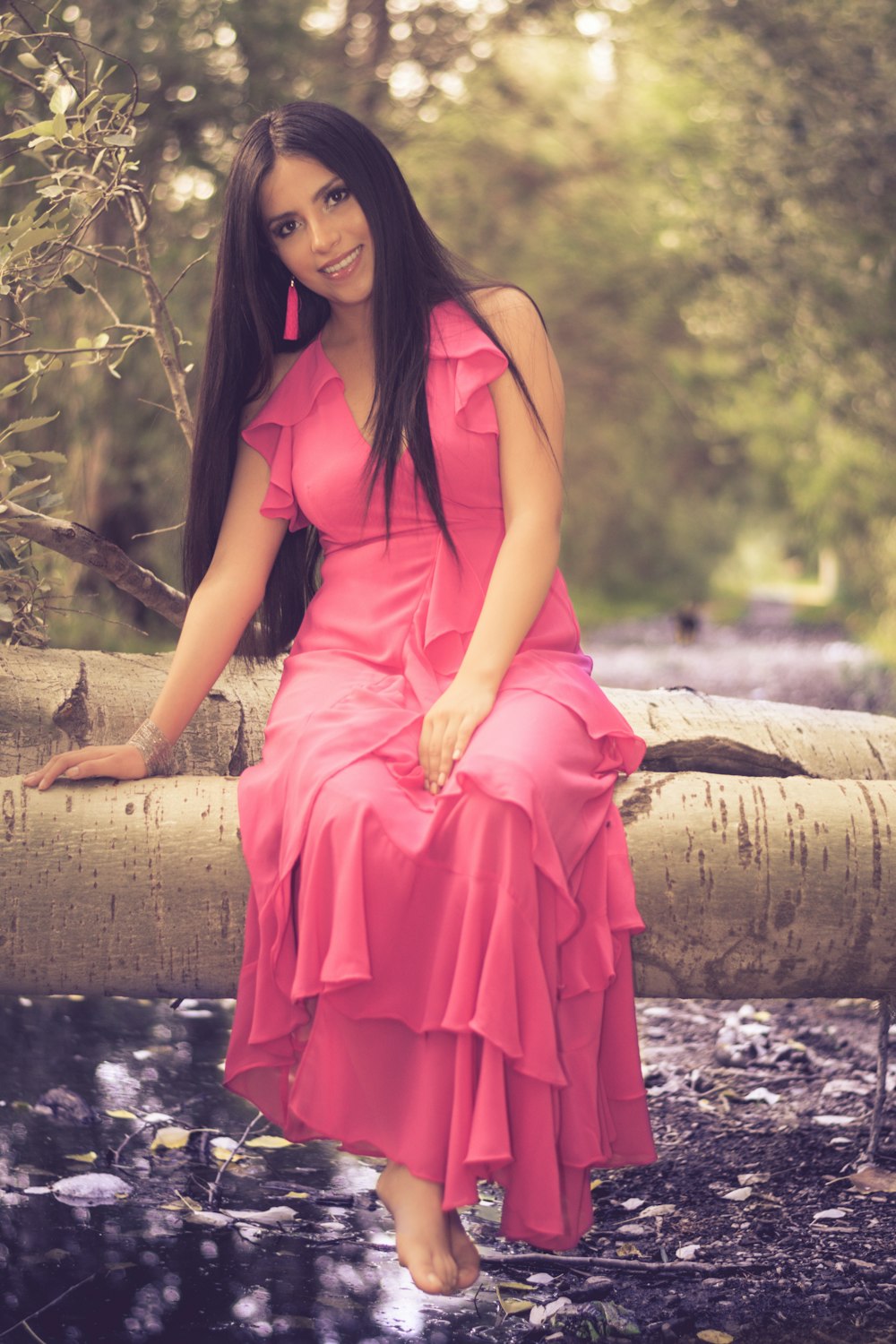 smiling woman wearing pink halter dress sitting on tree trunk during daytime