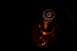 A close-up of a bottle cap with the label 'Blended Scotch Whisky'. The lighting highlights the cap's intricate design and the amber color of the liquid inside the bottle. The background is dark, emphasizing the top of the bottle.