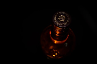 A close-up of a bottle cap with the label 'Blended Scotch Whisky'. The lighting highlights the cap's intricate design and the amber color of the liquid inside the bottle. The background is dark, emphasizing the top of the bottle.