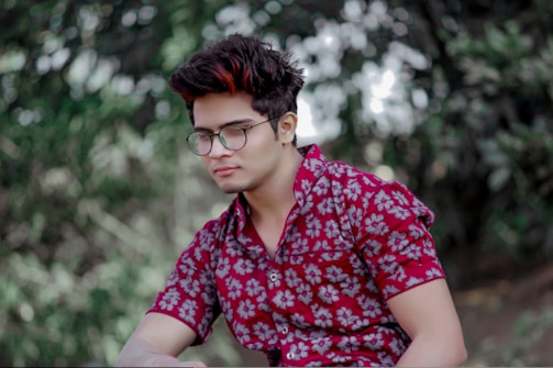 man wearing eyeglasses sitting near trees