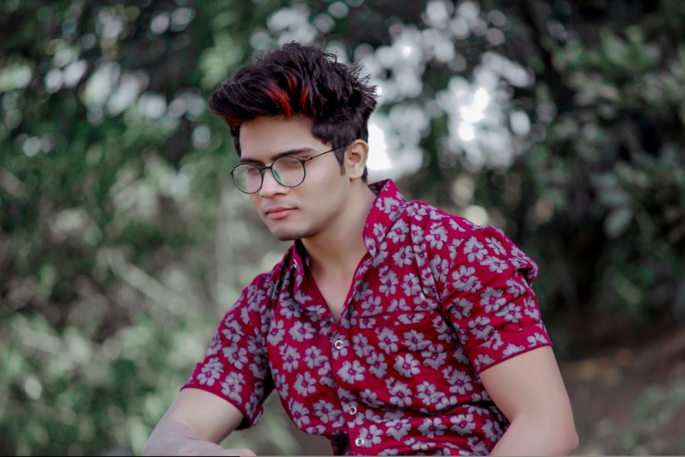 man wearing eyeglasses sitting near trees