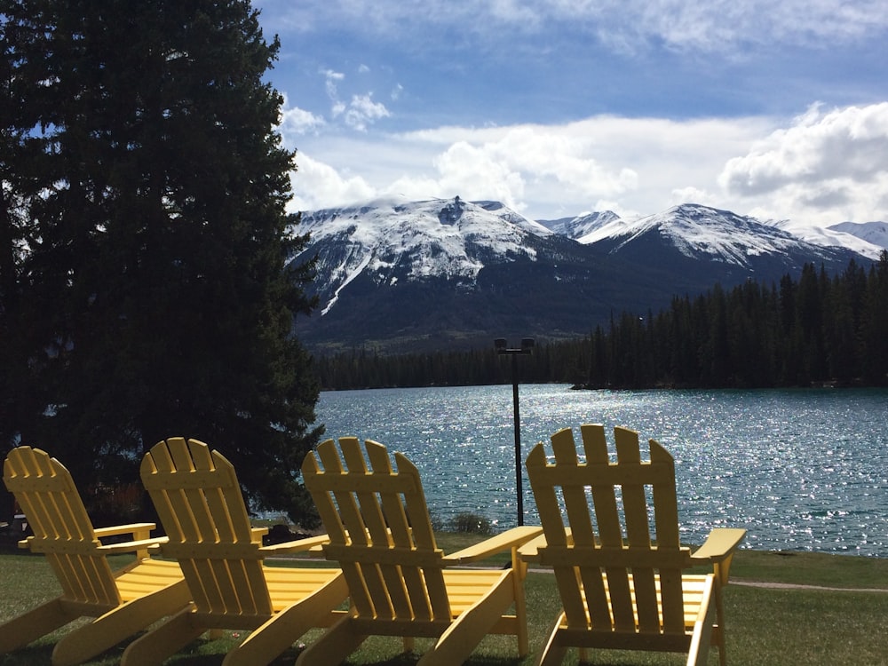 four yellow adirondack chairs near lake during daytime