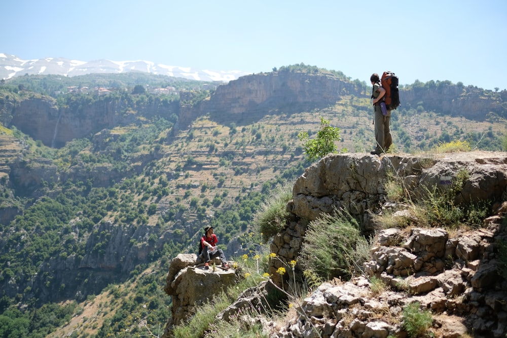 man standing on mountain in front of another man who seats during daytime