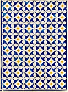 A geometric pattern composed of circular and diamond shapes in a grid format. Predominantly featuring dark blue and white circular designs with golden yellow diamonds at the intersections. The repetition of the pattern creates a visually striking and symmetrical design.