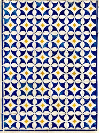 A geometric pattern composed of circular and diamond shapes in a grid format. Predominantly featuring dark blue and white circular designs with golden yellow diamonds at the intersections. The repetition of the pattern creates a visually striking and symmetrical design.