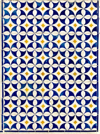 A geometric pattern composed of circular and diamond shapes in a grid format. Predominantly featuring dark blue and white circular designs with golden yellow diamonds at the intersections. The repetition of the pattern creates a visually striking and symmetrical design.