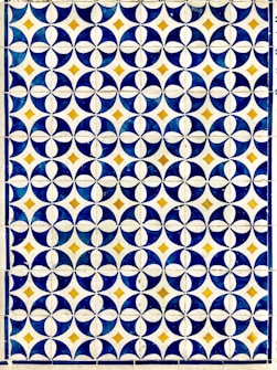 A geometric pattern composed of circular and diamond shapes in a grid format. Predominantly featuring dark blue and white circular designs with golden yellow diamonds at the intersections. The repetition of the pattern creates a visually striking and symmetrical design.