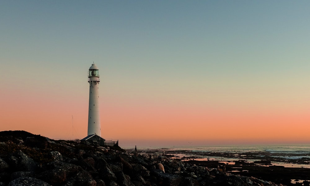 white lighthouse on hill in beach under orange sky at sunset