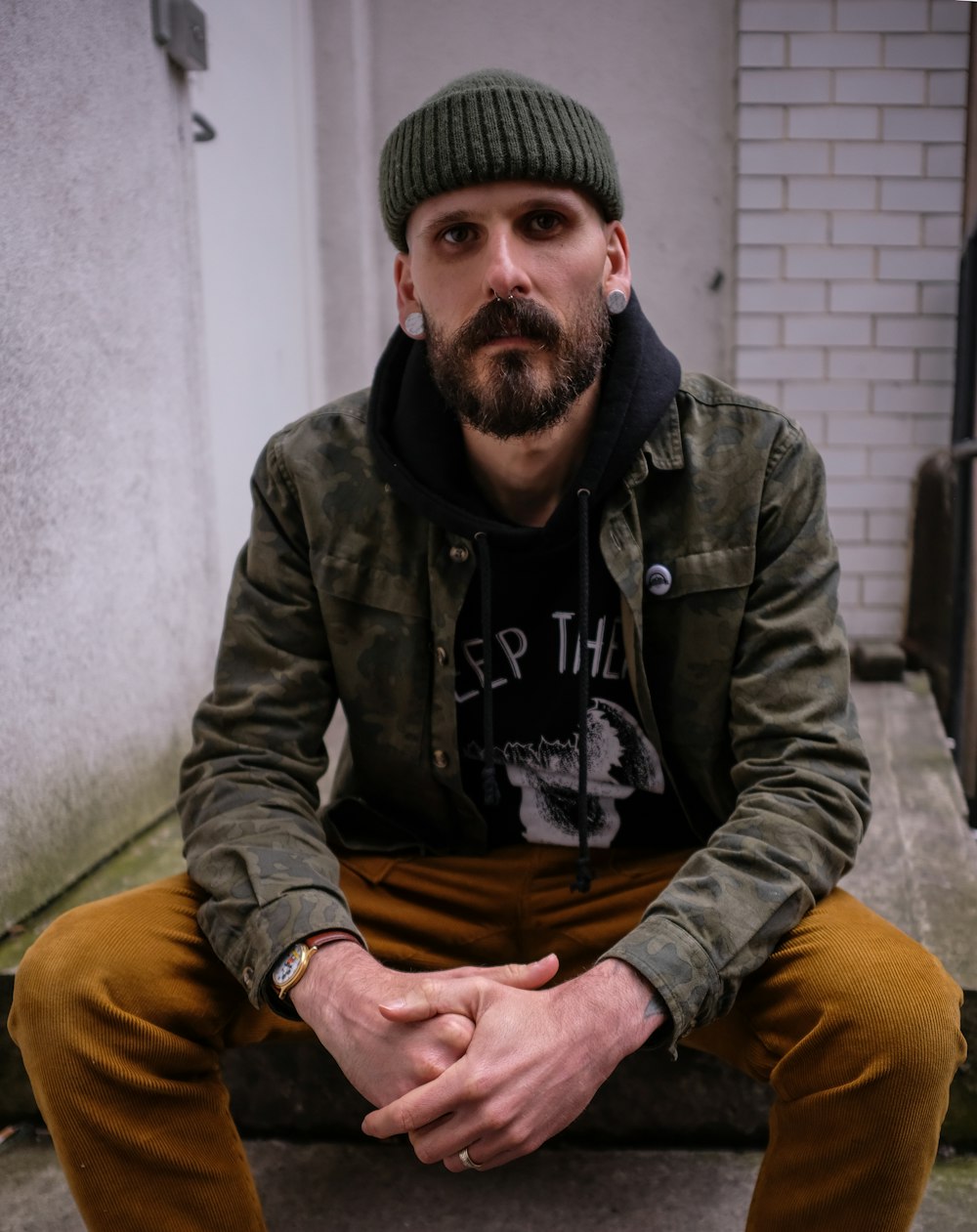 man wearing jacket seated near wall