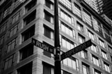 A black and white photograph features an intersection with street signs for N Rush St and E Superior St. The background shows the facade of a multi-story building with numerous windows and a modern architectural style.