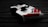 A video game controller with a sleek design, predominantly white with red and black accents. It sits on a dark wooden surface, with shadows enhancing its contours and details.