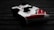 A video game controller with a sleek design, predominantly white with red and black accents. It sits on a dark wooden surface, with shadows enhancing its contours and details.
