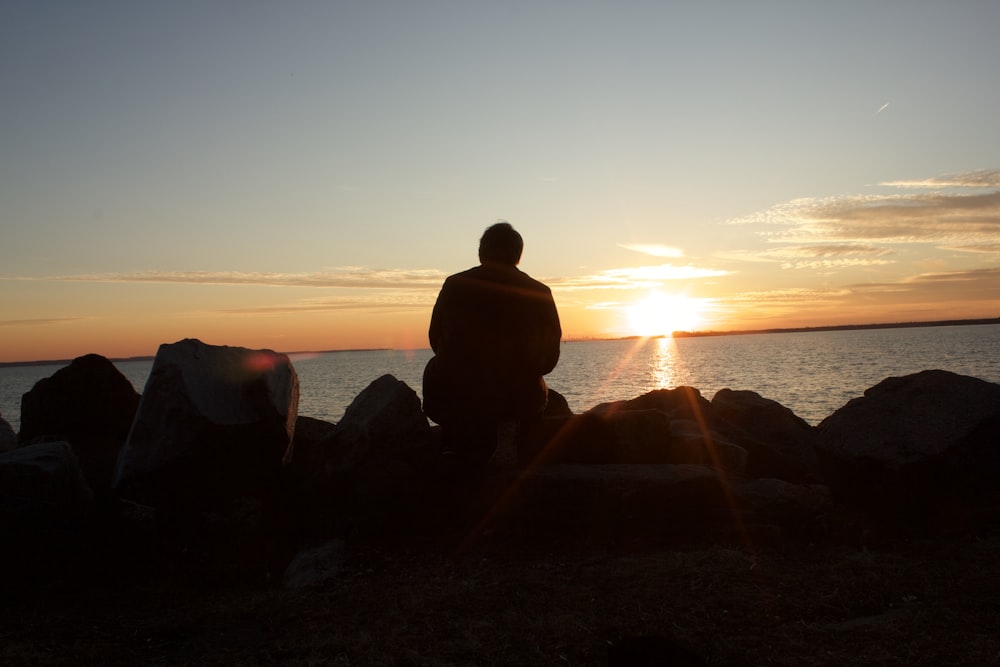 silhouette of man sitting on rock during sunset