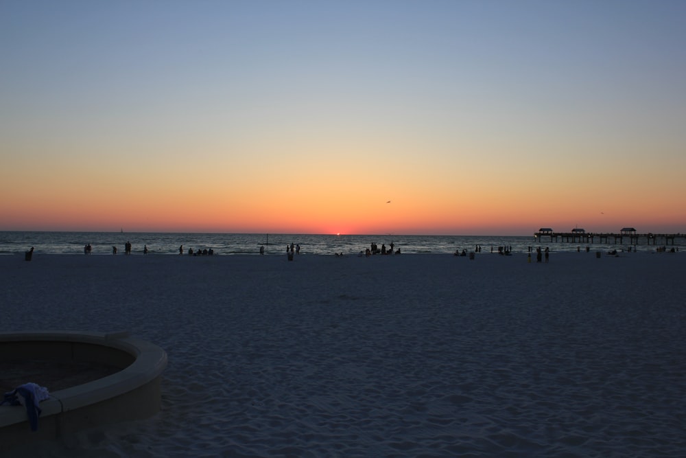 the sun is setting on the beach with people in the water