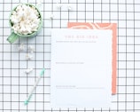 A flat lay composition features a green mug filled with popcorn, placed on a white and black grid-patterned surface. Next to the mug is a worksheet titled 'The Big Idea' with sections for describing a business concept. A mint green pen lies nearby, and some scattered popcorn pieces are visible on the grid.