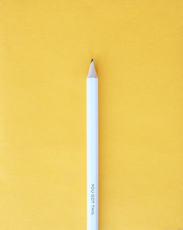A white pencil with the words 'YOU GOT THIS' engraved on it stands upright against a bright yellow background. The pencil's tip is sharpened and points upwards.