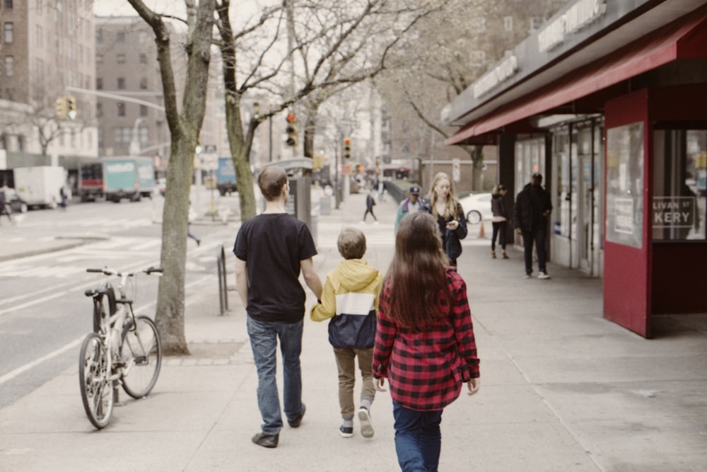 man in black t-shirt holding hands with child walking at the street