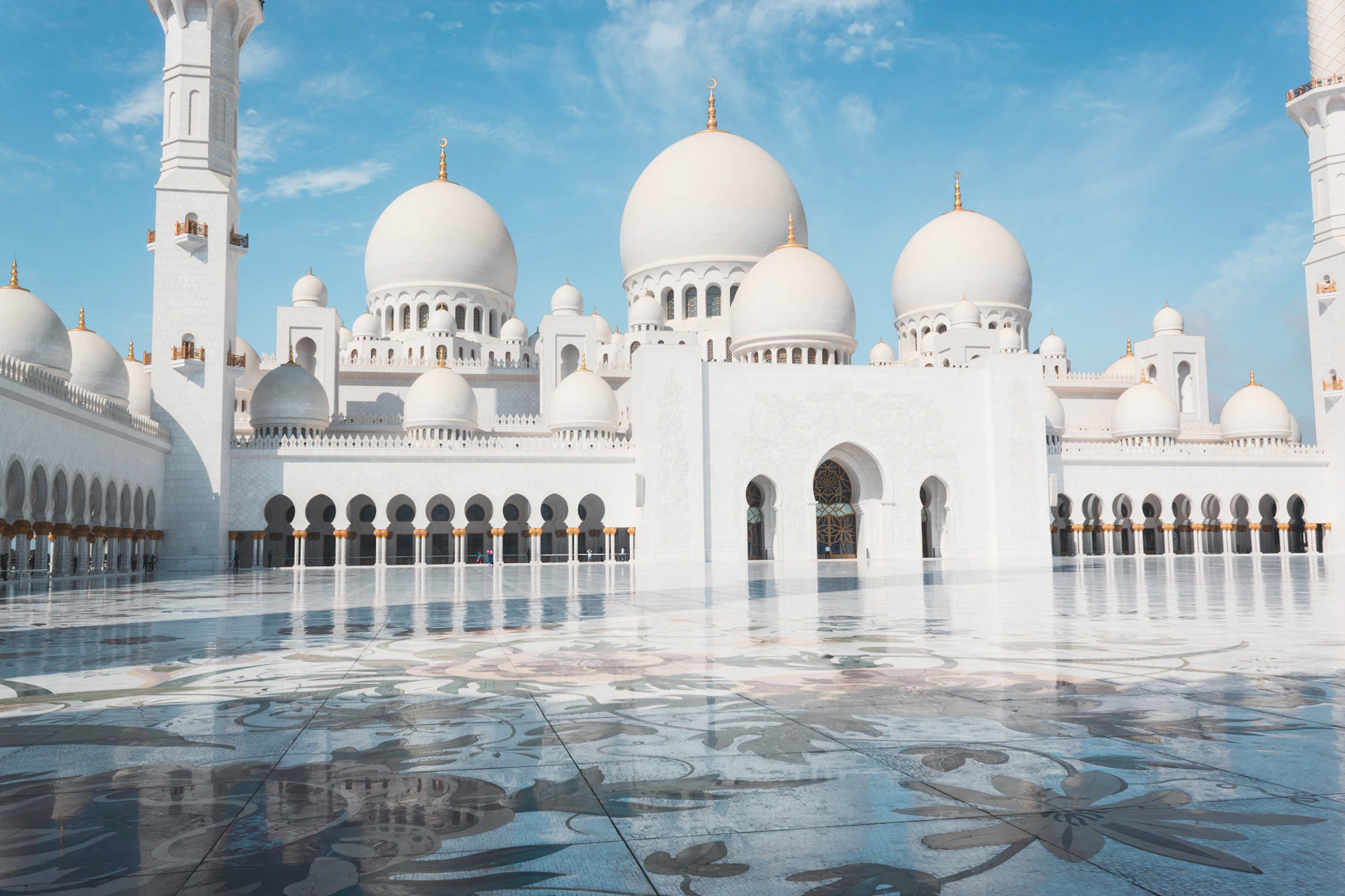 The white domes and reflective courtyard of Sheikh Zayed Grand Mosque in Abu Dhabi