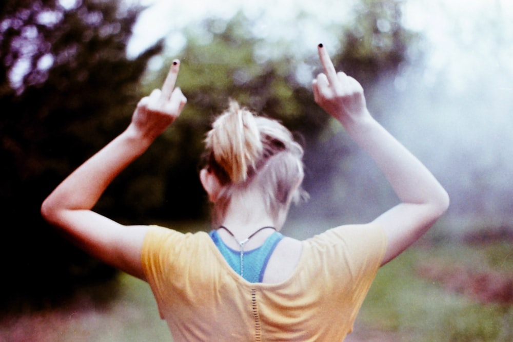 selective focus photography of woman wearing beige top holding out both middle fingers