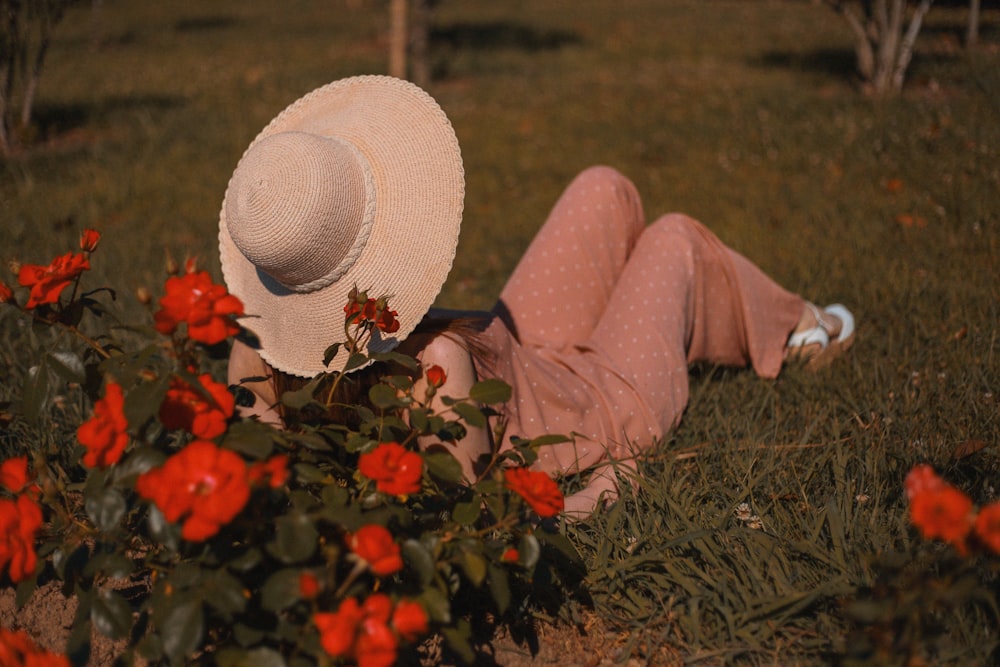 Mujer acostada en el campo de hierba verde junto a la planta de flores rojas