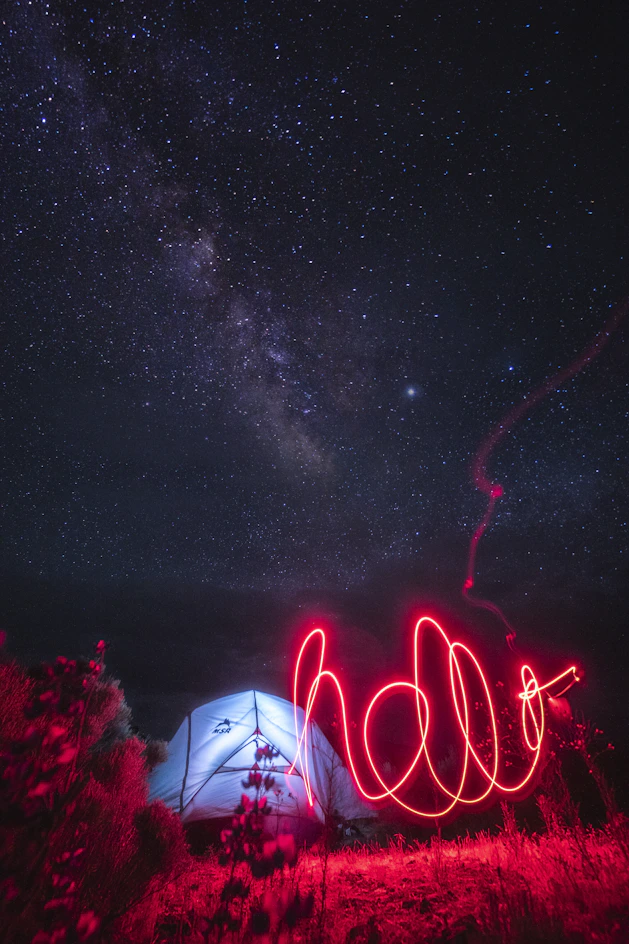 red light streak near lighted tent under starry night sky