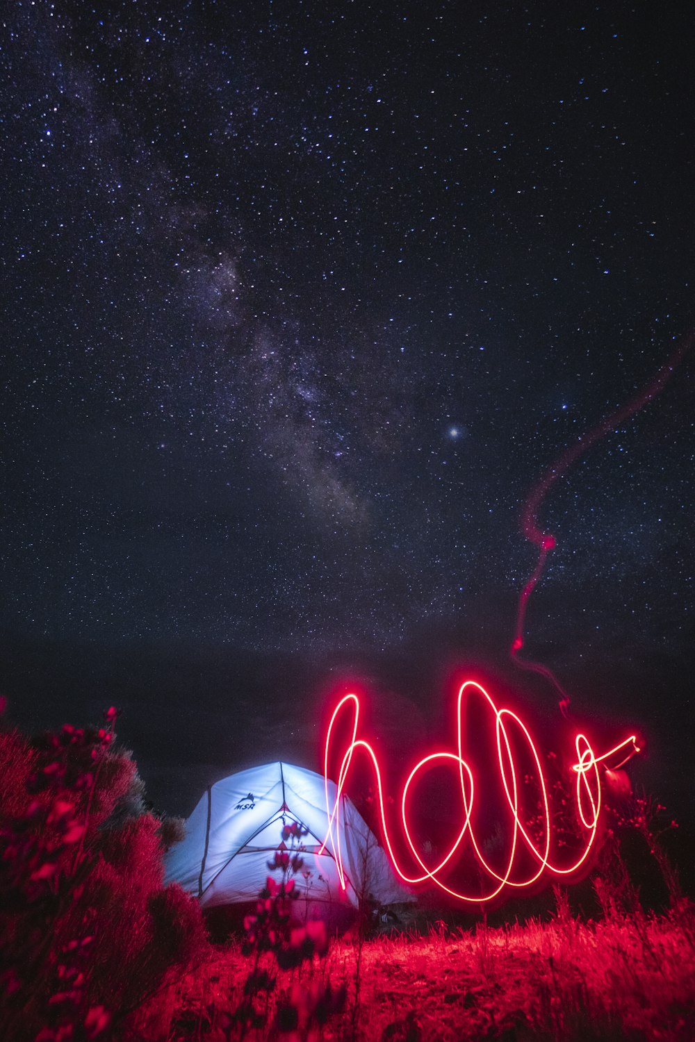roter Lichtstreifen in der Nähe des beleuchteten Zeltes unter dem Sternenhimmel