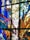 A section of stained glass art featuring a mix of vibrant colors. The design includes decorative elements such as leaves, wheat stalks, and possibly religious motifs. The artwork is arranged in abstract sections with geometric borders.