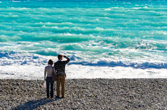 A couple laughing together on a sandy beach with turquoise waves gently rolling in.