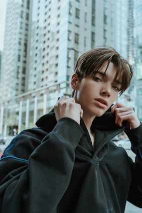 A close-up shot of a young adult wearing a sleek black Nisqala hoodie against a muted urban backdrop.