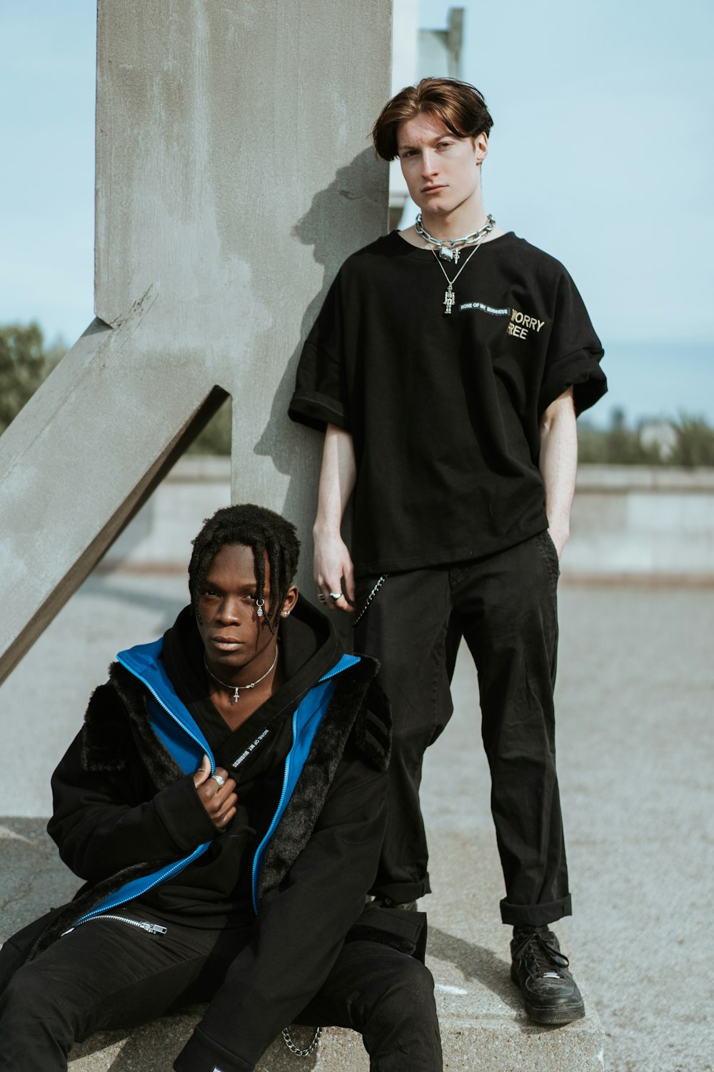 selective focus photography of standing man in black shirt and pants behind sitting man wearing black and blue jacket and black undershirt