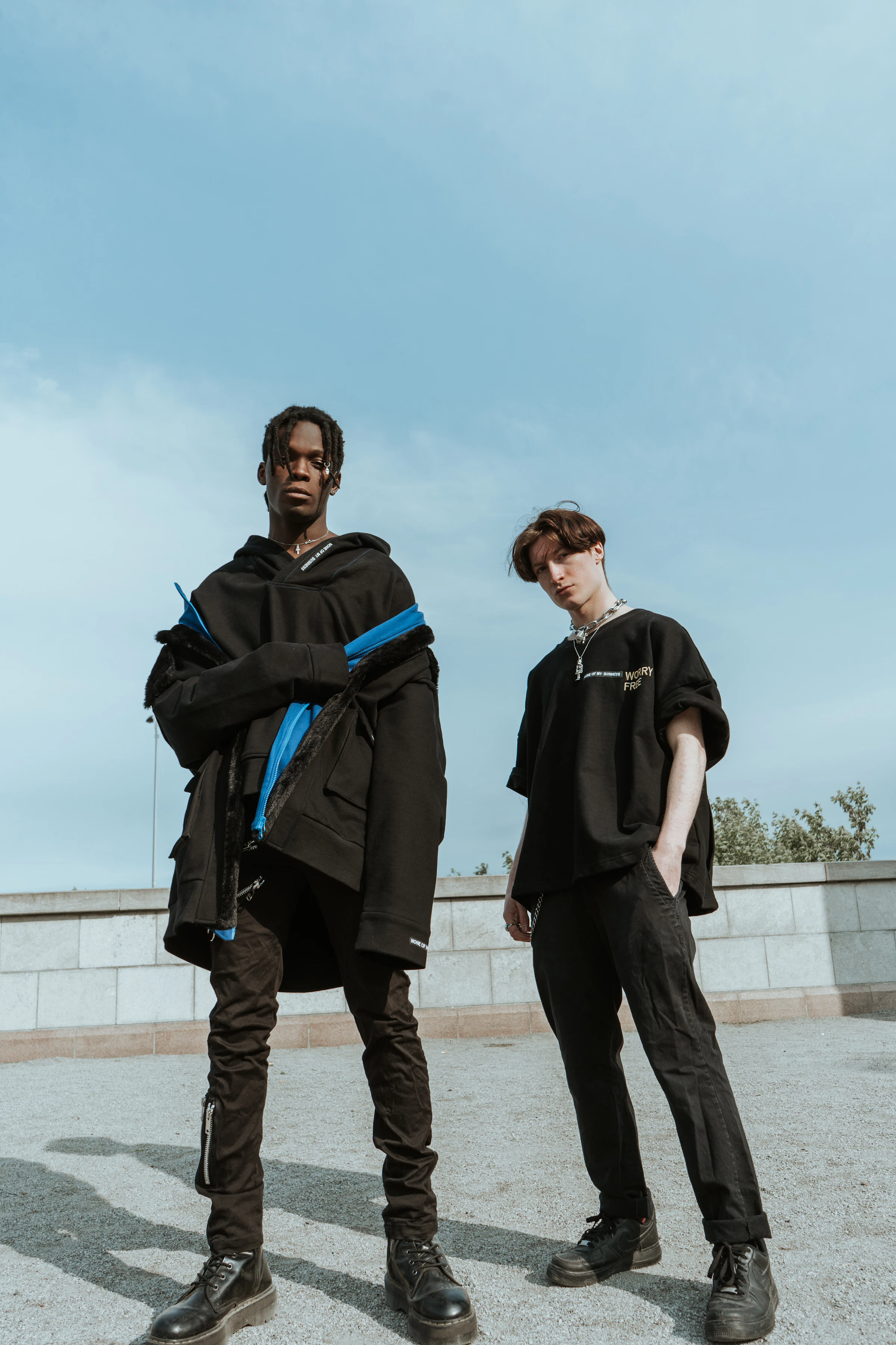 Two models in black oversized streetwear under a blue sky