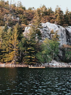 A canoe gliding across a crystal-clear river framed by towering evergreens and rocky cliffs.