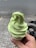 A hand holds a soft serve ice cream cone with a light green swirl against a background of a tiled pavement and a blurred street.