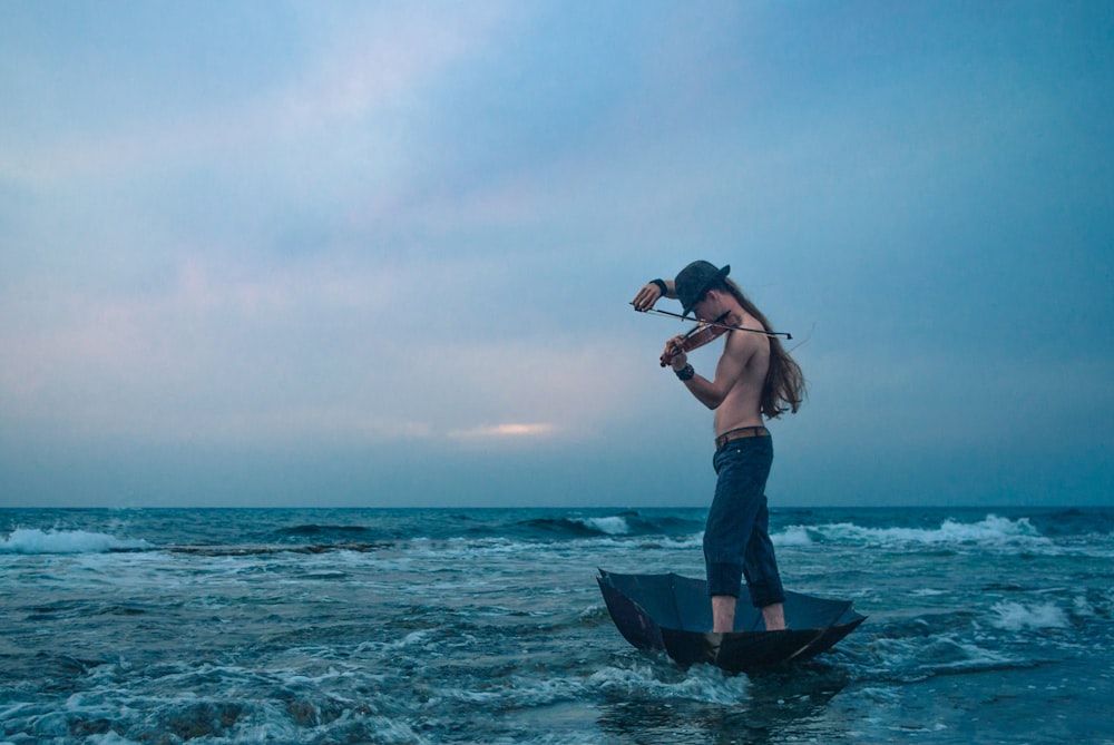 person wearing blue jeans riding boat playing violin