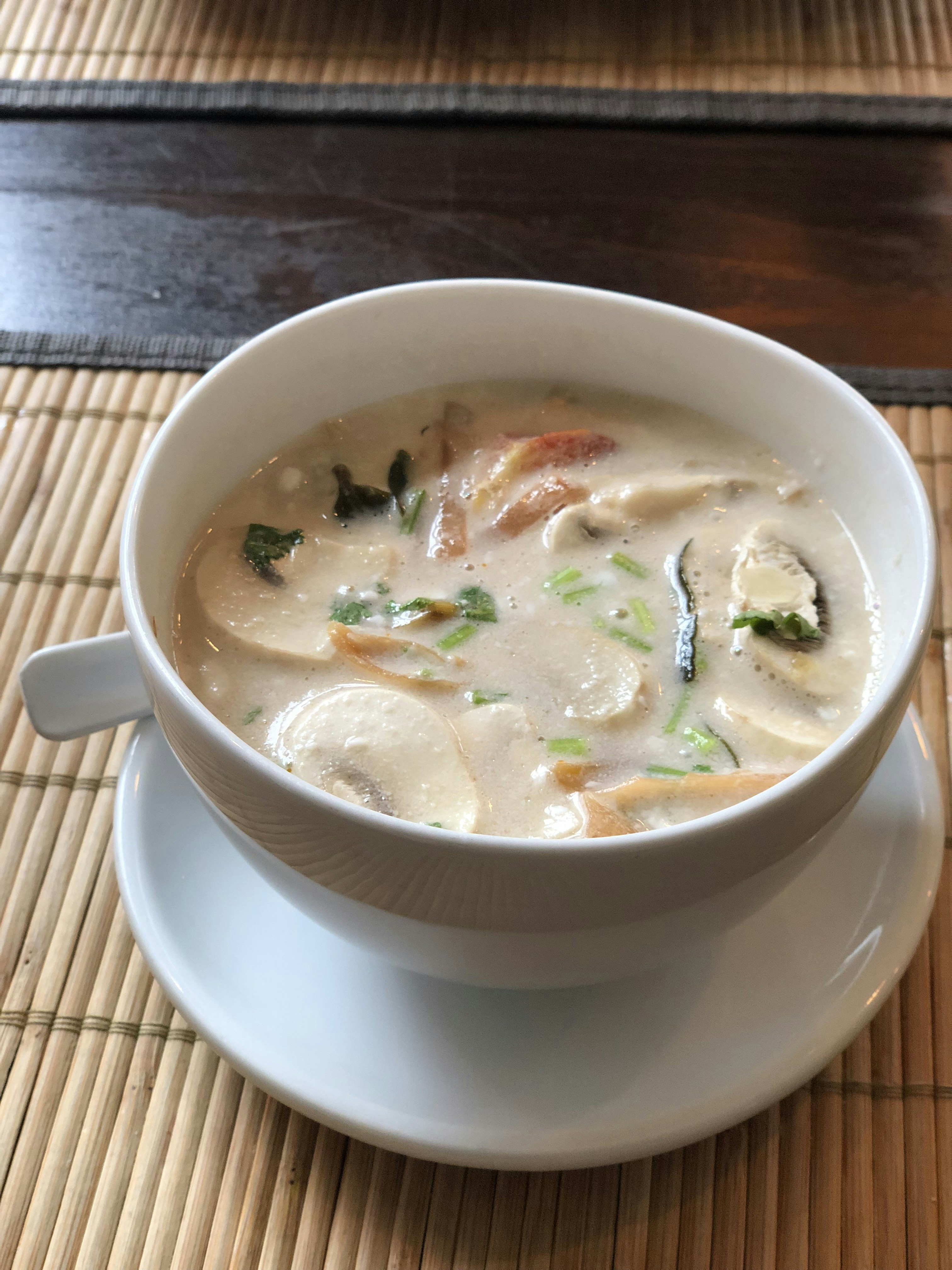 Creamy mushroom soup in a white ceramic bowl with fresh herbs and bread, cozy warm lighting