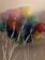 A cluster of colorful balloons with white strings attached, floating indoors against a light-colored ceiling.