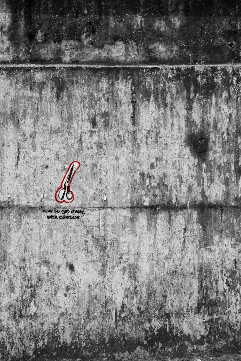 a black and white photo of a red scissors on a concrete wall