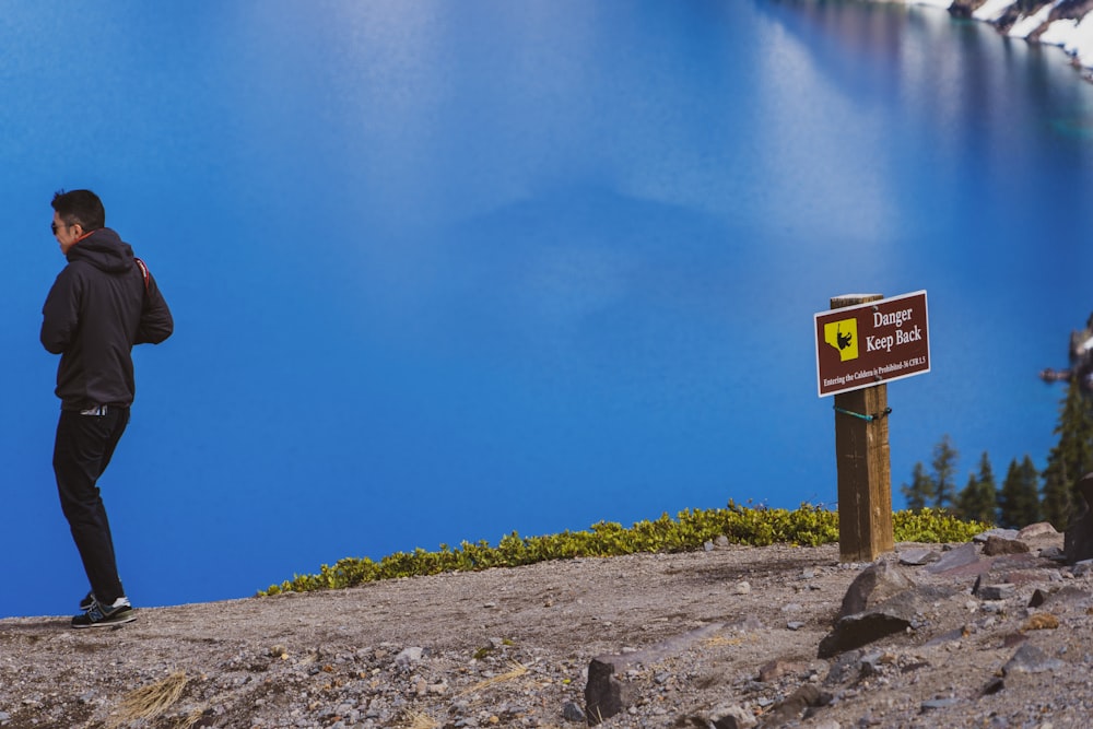 man walking away from danger keep away signage by the blue lake