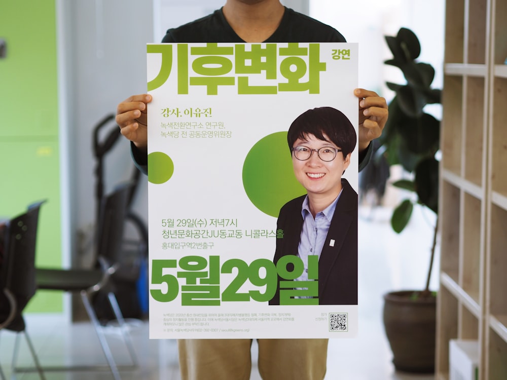 standing person holding poster with smiling man photo and Hangul texts