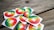 A collection of stickers and buttons featuring a rainbow gradient background with white text in a non-Latin script placed on a wooden surface.