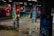 Vivid graffiti art covers multiple concrete pillars in an underground space, featuring a variety of colorful and intricate designs, including faces, abstract shapes, and lettering. The floor is reflective with small puddles, adding to the dynamic and urban atmosphere of the setting.
