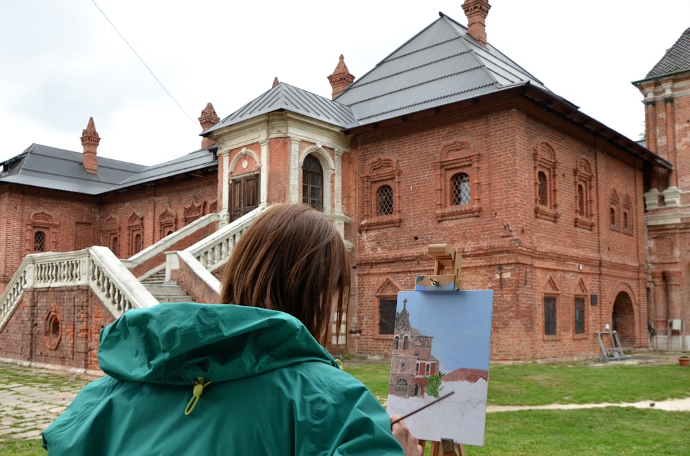 woman wearing teal hoodie painting brown building during daytime