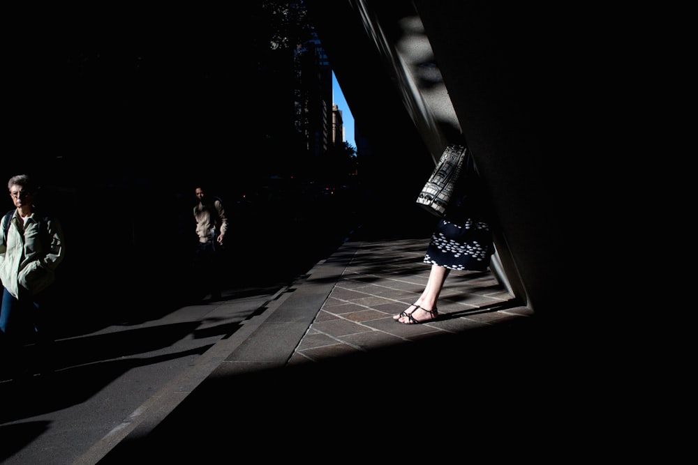 woman sitting beside building in front of man walking on pavement