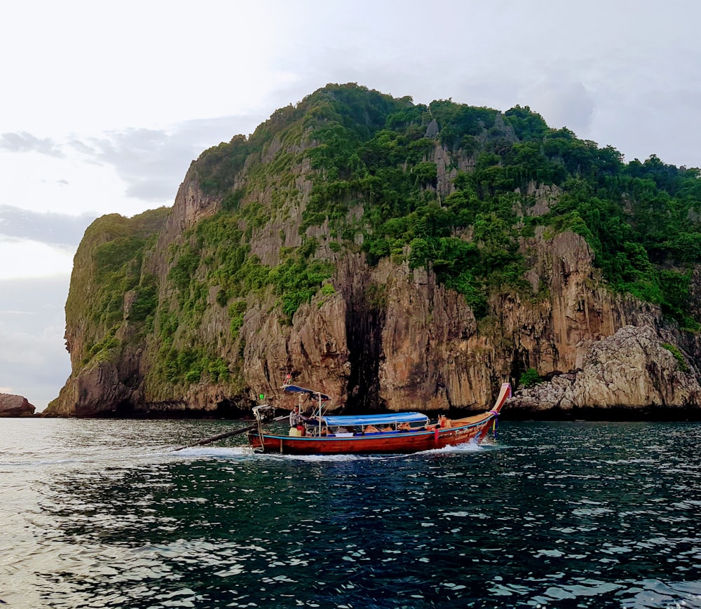 red boat on body of water near brown cliff during daytime