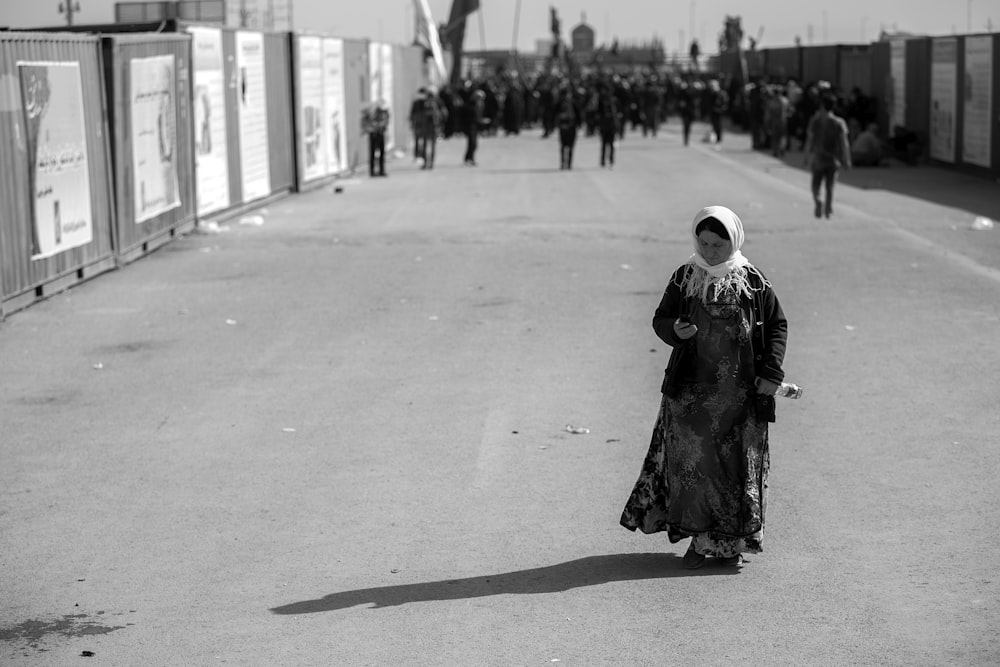 grayscale photo of woman wearing abaya dress walking street