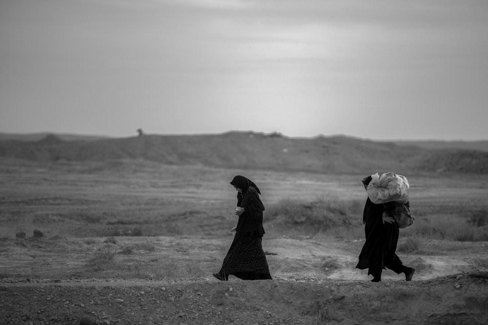 a couple of women walking across a dirt field