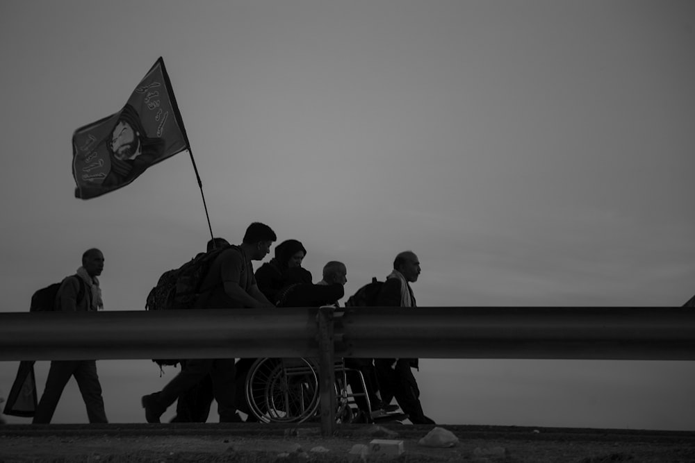 grayscale photo of people walking on street while holding flag