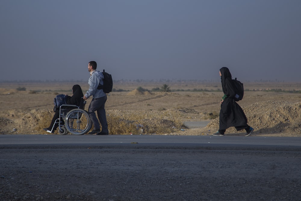 man carrying black backpack pushing wheelchair