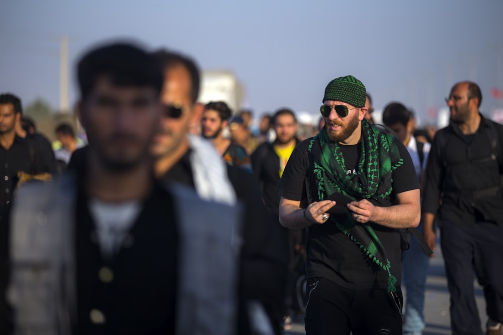 selective focus photography of man wearing sunglasses walking between people near outdoor during daytime